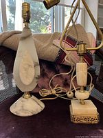 Two vintage marble and brass table lamps displayed side by side on a chair. Teardrop and square base shapes evident.