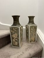 Two matching ceramic floor vases shown on carpeted stairs, featuring square base and detailed floral reliefs on all sides.