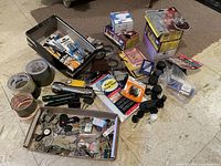 Wide view of all items including keys in a box, batteries in packets and loose, three rolls of tape, flashlights, black rubber chair stoppers, and various small items scattered on floor.