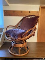 Rattan swivel chair with purple cushions, showing side and front angles.