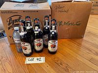 Photo of several reusable beer bottles from Hacker-Pschorr with swing-top ceramic stoppers and cardboard boxes in the background, labeled as lot 42.