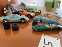 Photo showing six vintage slot cars in varying conditions with additional tires and a racing spoiler.