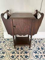 Front view of wooden smoker's table, showing carved decorative panels, side handles, turned legs, and a lower shelf.