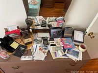Wide view of assortment of stationery including vintage calculators, greeting cards, pencil sharpener, glue stick, and other items on wooden dresser with mirror.