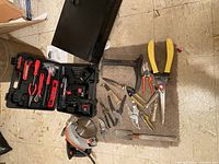 Additional hand tools laid out next to the cordless drill set including hammer, multiple pliers, cutters and metal shear, and a portable black CD player.