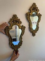 Two ornate mirrors held side by side on a wall showing matching baroque style plaster frames in gold finish.