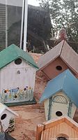 Photograph showing multiple painted wooden bird houses on a wooden surface with visible reflection of a person taking the photo.
