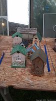 Five assorted birdhouses on a plywood surface in outdoor setting captured to show variety and condition.