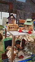 Outdoor photo of multiple bird houses, wooden planters, small pots, and garden decor arranged on and around a wooden pallet table.
