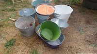 Eight assorted buckets in different sizes and colors placed outdoors on dry grass background
