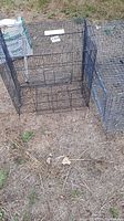 Three weathered wire bird cages on dry grass ground. One large cage and two smaller cages with wire mesh doors visible.