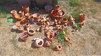 Wide shot showing large assortment of terracotta pots and yard art on grass with dry patches.