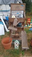 Full view of wooden fruit crate display shelf with garden items including watering cans, bird houses, flower pots, wooden yard art pieces, and the WATERING CANS sign.