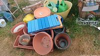 Photo showing a mix of plastic pots, garden seat, watering cans, and trays on grass outdoors