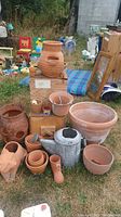 Overview of lot showing multiple terracotta pots, metal watering can, and wooden birdhouse outdoors on grass