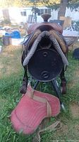 Rear view of western leather saddle mounted on stand with both saddle blankets visible underneath and in front on grass.
