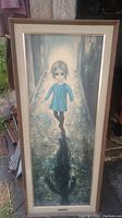Full view of framed painting showing child in blue dress walking in alleyway.