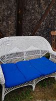 Front view of white wicker loveseat with blue cushion placed outdoors showing woven design and condition