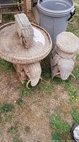 Wicker elephant tables on grass with round glass tops and elephant base details.