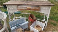 Front view of white wicker table showing wooden top and drawer, surrounded by baskets under and around it.