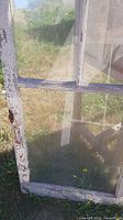 Close-up front of window with three vertical glass panes and weathered white wooden frame showing chipped paint and rust on hinge area.
