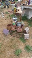 Full view of various outdoor yard art items placed on and around an old metal TV tray on grass, including multiple birdhouses, metal planters, and garden sculptures.