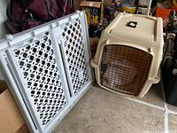 Image showing beige plastic animal carrier crate with black metal front cage door and white plastic folding pet gate.