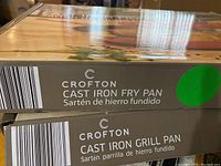Boxes labeled Crofton Cast Iron Fry Pan and Cast Iron Grill Pan stacked, showing brand and product type