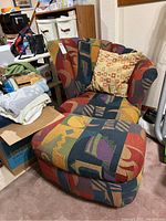 Photo showing chair with clam shell fabric multicolored upholstery, ottoman, and throw pillow in a cluttered room.