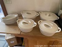 Full set showing four covered pans of varying sizes and four oval ceramic serving dishes.