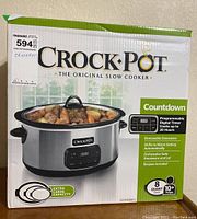 Box front with product image showing stainless steel oval slow cooker with digital timer and 8 quart capacity.