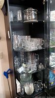 Cabinet shelf holding various glassware including pitchers, mugs, glasses, and bowls.