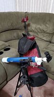 Blue and white telescope mounted on black tripod in front of a red and black carry bag