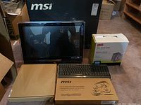Overview of lot showing MSI all-in-one PC, MSI keyboard box, HP keyboard, and box of Fellowes jewel cases