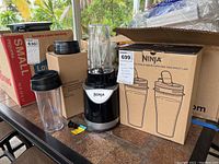 Ninja single serve blender components on table including blender base, blending cups, and box with additional cups and lids