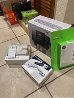Photo showing the Canon Selphy CP1300 printer box, Polaroid EVA case, car chargers grouped together on tiled floor.