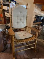Front view of wooden rocking chair with beige tufted cushions, showing scratches and wear on wood and cushions.