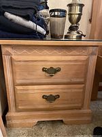 Front view of one light wood end table showing carved design, two drawers with brass handles.