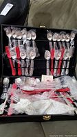 Overview of flatware set inside a black case, pieces mostly wrapped in plastic and bubble wrap.