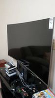 Front angle view of curved screen TV on stand with remote and game cases on shelf