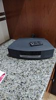 Front angled view of black Bose Wave Radio/CD player with remote on top, showing overall shape and condition.