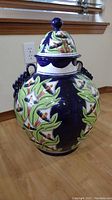 Full view of the blue ceramic floor vase with floral patterns and lid, showing overall design and size relative to the floor.