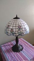 Full view of stained glass lamp on striped cloth showing domed shade with geometric and floral stained glass design.