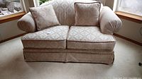 Front view of ivory and gold damask upholstered love seat with rolled arms and two throw pillows