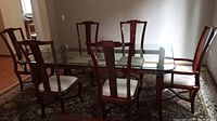 Full view of glass-topped dining table on rug with matching chairs
