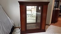 Full front view of the mahogany display cabinet showing glass central door, veneer decorated side panels, and crown molding top.