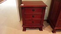 Front view of one solid mahogany nightstand showing three drawers with drop ring pulls and carved details.