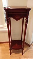 Full view of the tall mahogany pedestal plant stand showing the turned legs and veneer inlay design on the top and bottom surfaces.