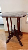 Full side view of mahogany wood table base with marble top placed on it.