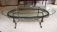 Full view of oval glass top coffee table showing metal base structure including legs and connecting rods.